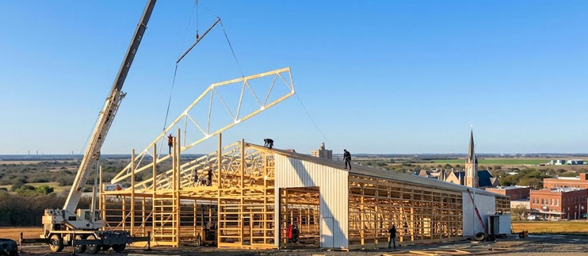 Hydraulic crane hoisting a clear-span wood roof truss onto an active commercial jobsite in Victoria County, TX.